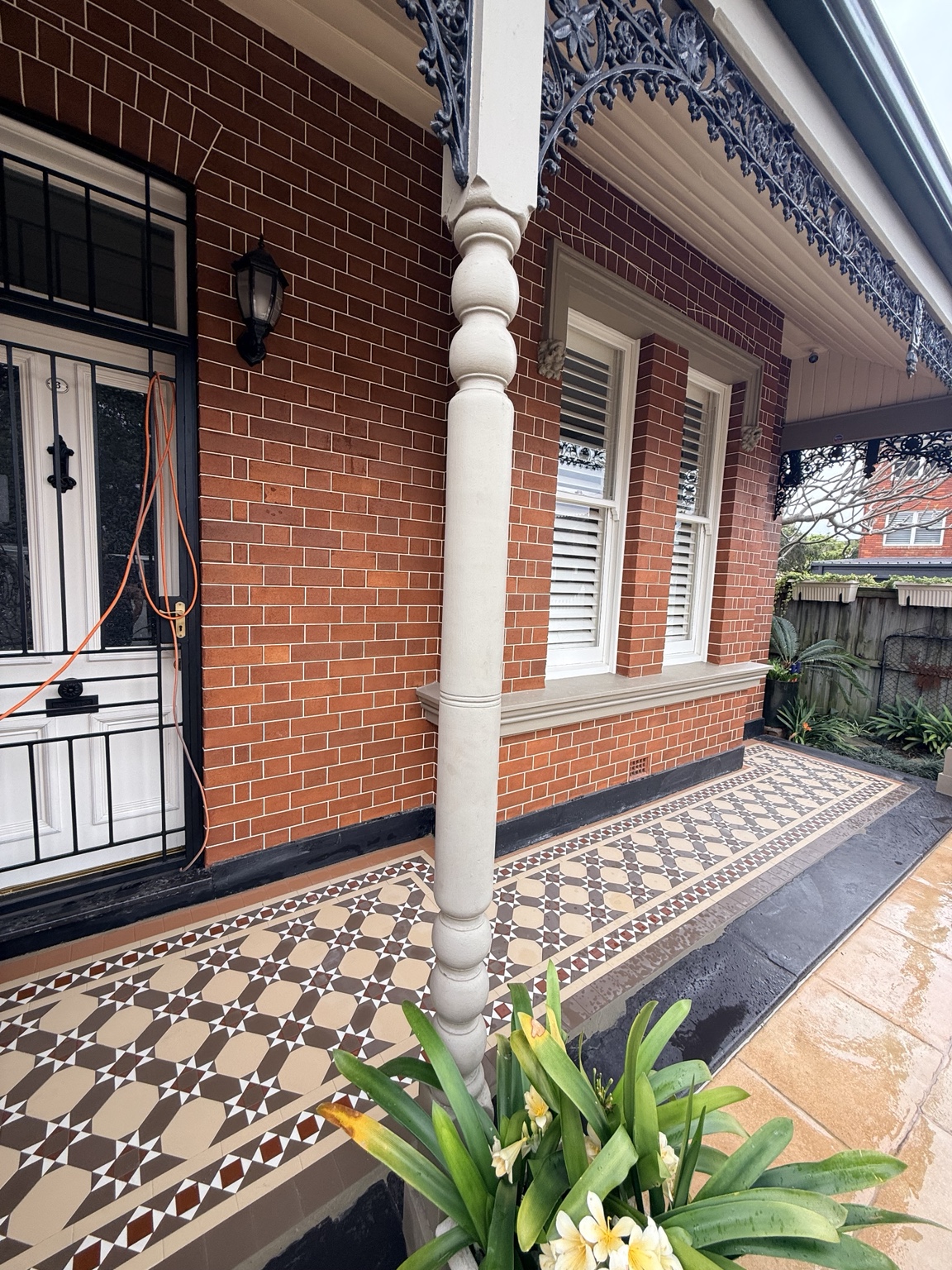 Charcoal, oatmeal, red and white tessellated tiles beside a verandah post and brick wall in Drummoyne